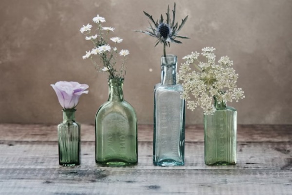 Four glass bottles in different sizes with beautiful flowers placed in each one.